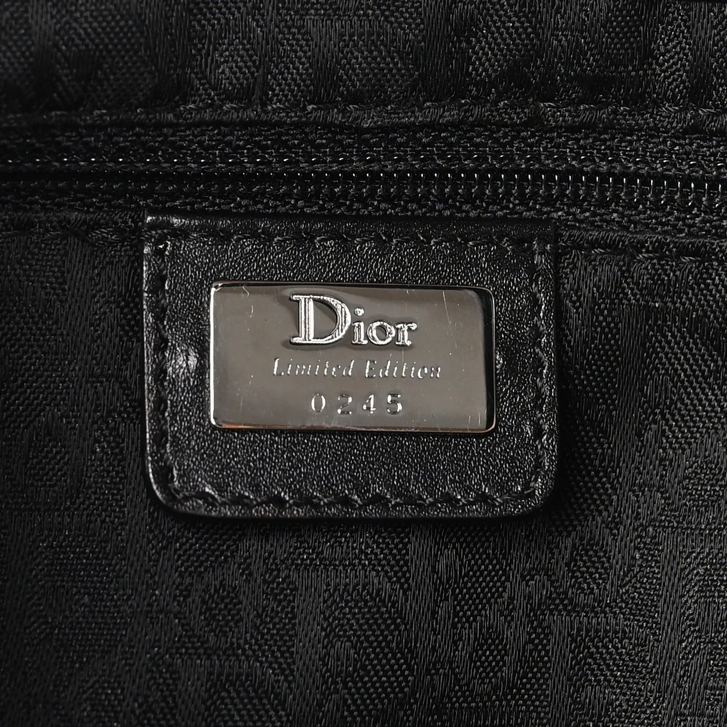 Close-up of a black Dior Limited Edition bag featuring a silver-tone metal logo plate on a textured black fabric background.